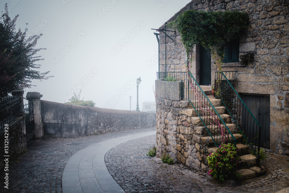 Stone houses in Monsanto, Portugal, shrouded in mist on a foggy autumn day, creating a mystical and atmospheric scene.