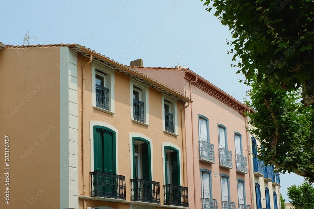 Rustic nostalgic facades with windows and balconies of soft colours seen through greenery in France Rustic nostalgic facades with windows and balconies of soft colours seen through greenery in France