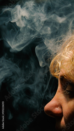White vape smoke billows against a dark background, while a close-up profile shows the woman's closed eyes, blonde hair and nose. The lighting creates a dramatic contrast between smoke and skin.