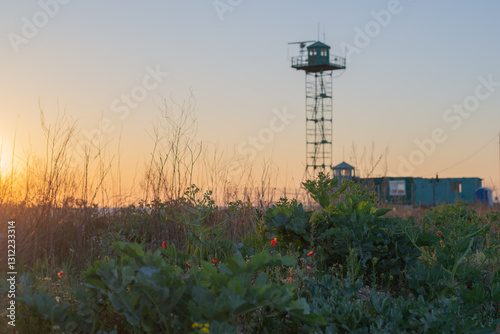 border observation tower military with radar and antenna at sea shore with beach and red flowers High quality photo