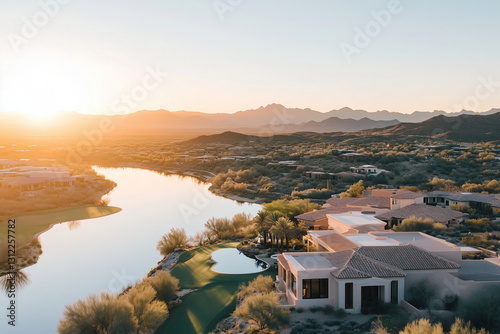 Aerial view of a luxurious desert home overlooking a serene lake at sunset, surrounded by lush greenery and arid mountains.

