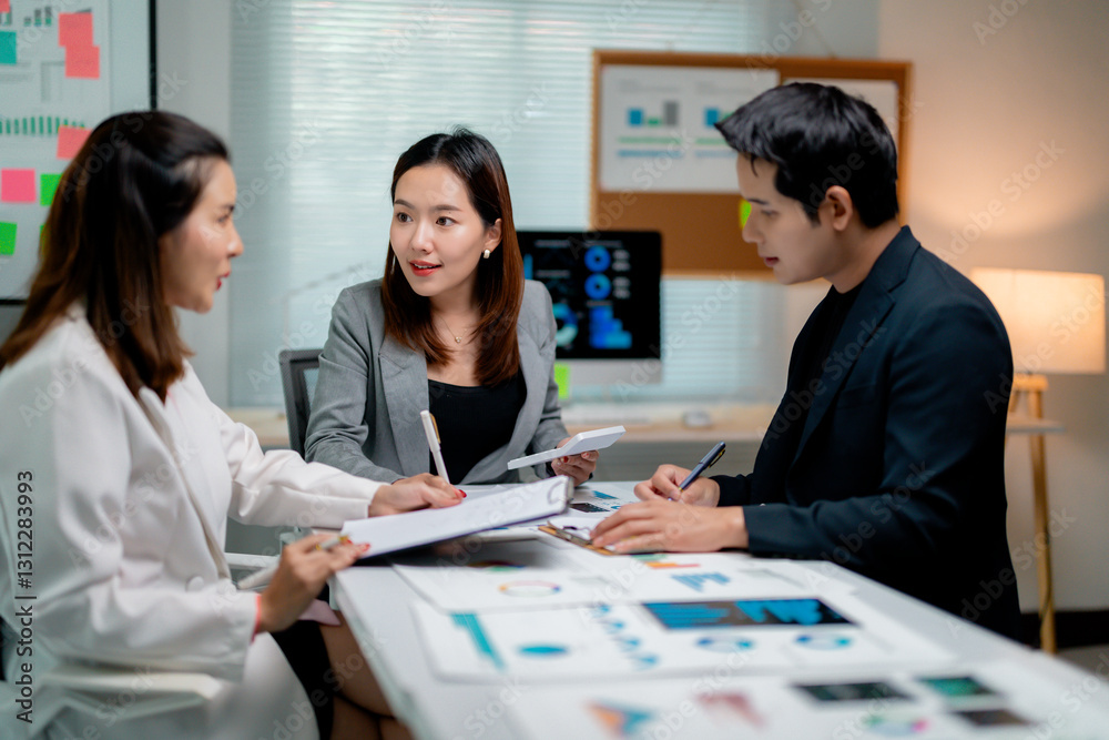 Fototapeta premium Asian businesspeople working together in modern office analyzing financial reports and discussing company strategy