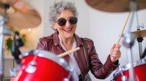 Elderly caucasian female drummer in leather jacket playing red drum kit.