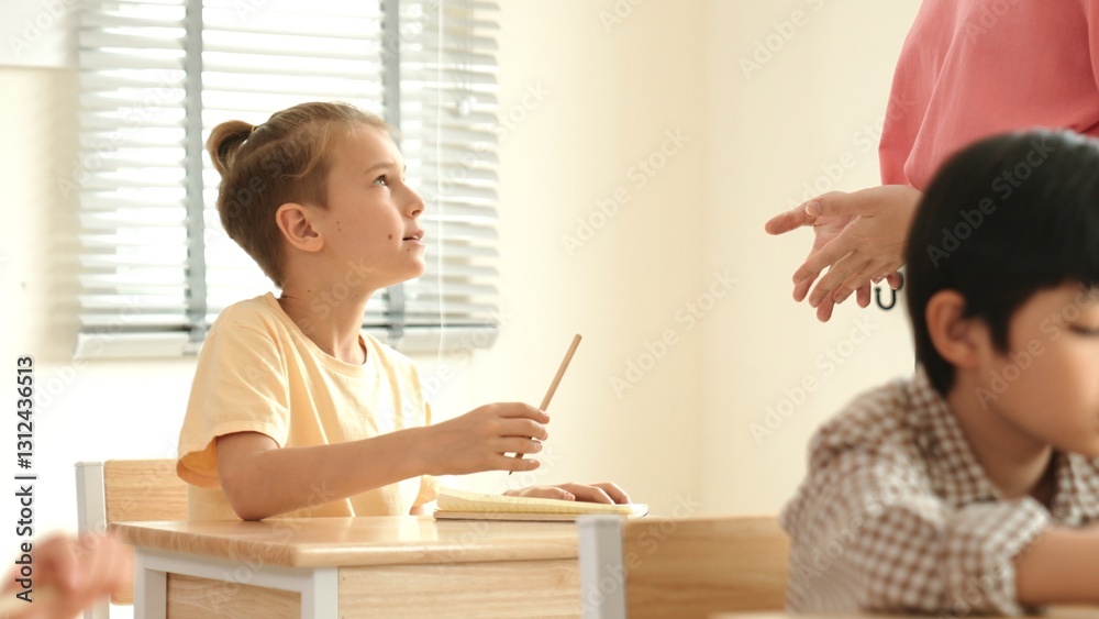 Beautiful teacher explaining test while caucasian boy doing classwork and listening explanation. Cute child looking at teacher while taking a notes or writing answer in paper at classroom. Pedagogy. Beautiful teacher explaining test while caucasian boy doing classwork and listening explanation. Cute child looking at teacher while taking a notes or writing answer in paper at classroom. Pedagogy.