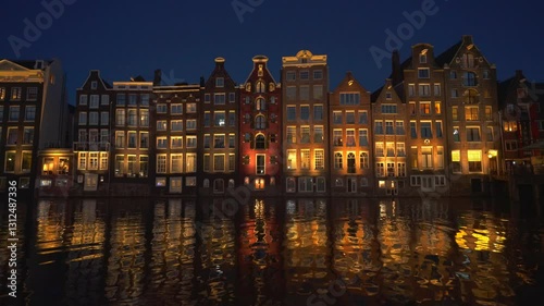 Amsterdam Damrak Canal Dancing Houses Lit Up at Night. Reflective Water Wide Low Angle 4K High Quality Color Corrected..