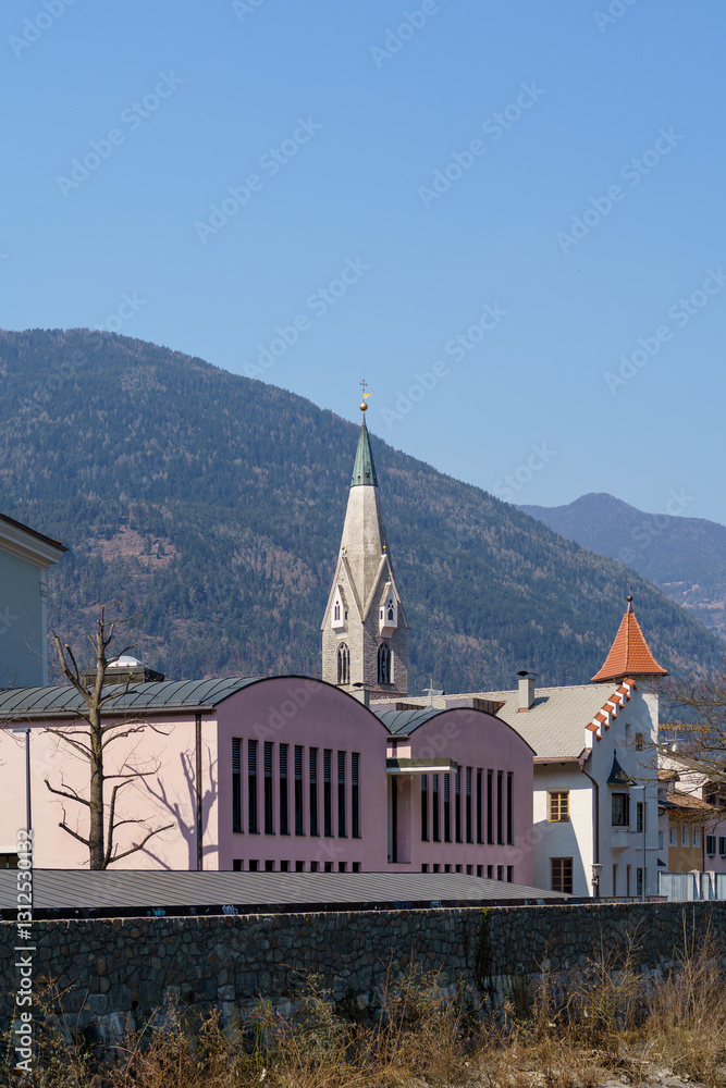 Fototapeta premium Brixen's Iconic Church Steeple with Modern and Historical Architecture in Alpine Setting