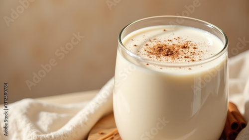 A glass of milk topped with cinnamon and a cookie on a wooden table.