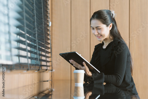 Fotografia Focused Professional: An elegant woman in a professional setting, engrossed in her tablet, embodies modern productivity and effortless focus, underscored by natural light and a touch of caffeine