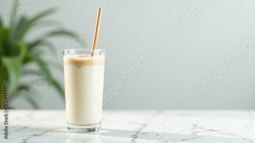 A creamy beverage served in a clear glass with a straw and a wooden stirrer on a white marble surface.