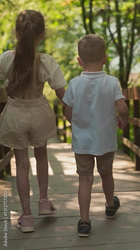 Little girl and boy hold hands walking together along viaduct in forest. Happy children enjoy travel to shady summer park. Kids explore nature jumping Little girl and boy hold hands walking together along viaduct in forest. Happy children enjoy travel to shady summer park. Kids explore nature jumping