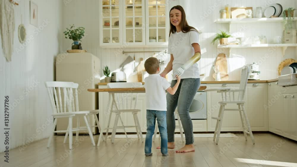 Young mom with prosthesis teaches little preschooler son to dance in modern kitchen Young mom with prosthesis teaches little preschooler son to dance in modern kitchen