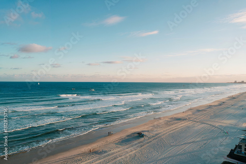 Vast ocean waves gently lap at the sandy shore under a serene sky at sunset
