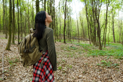 Young female hiker with a backpack breathing in the fresh air, savoring the beauty of the lush green forest while enjoying her outdoor adventure in nature's tranquility