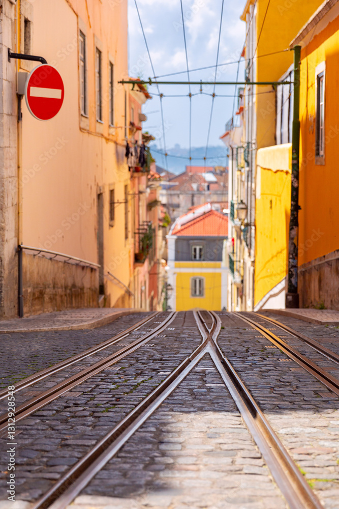 Tram tracks on a steep cobbled street in Lisbon, Portugal, surrounded by colorful traditional buildings and views of the city in the distance