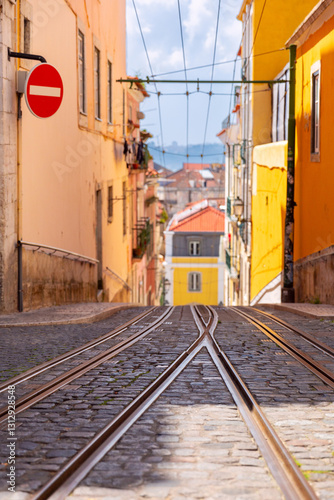 Obraz na płótnie Tram tracks on a steep cobbled street in Lisbon, Portugal, surrounded by colorful traditional buildings and views of the city in the distance w salonie