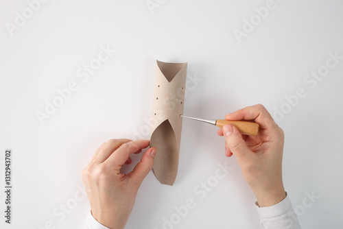 Canvas Print One hand is holding the tube, while the other hand is using awl to punch holes into the cardboard