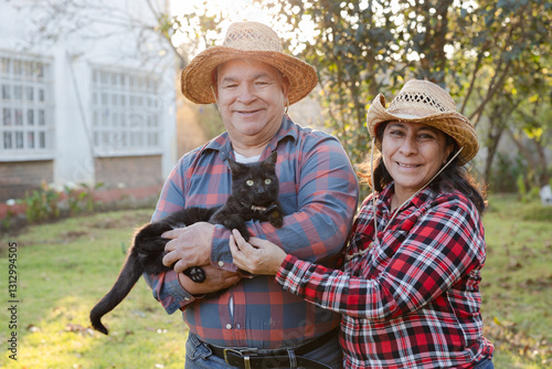 Senior hispanic couple happy with their black cat in their backyard - happy grandparents on their farm
