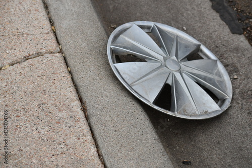 Fototapeta Naklejka Na Ścianę i Meble -  Unbranded hubcap on side of road. Hubcap leans up against sidewalk.