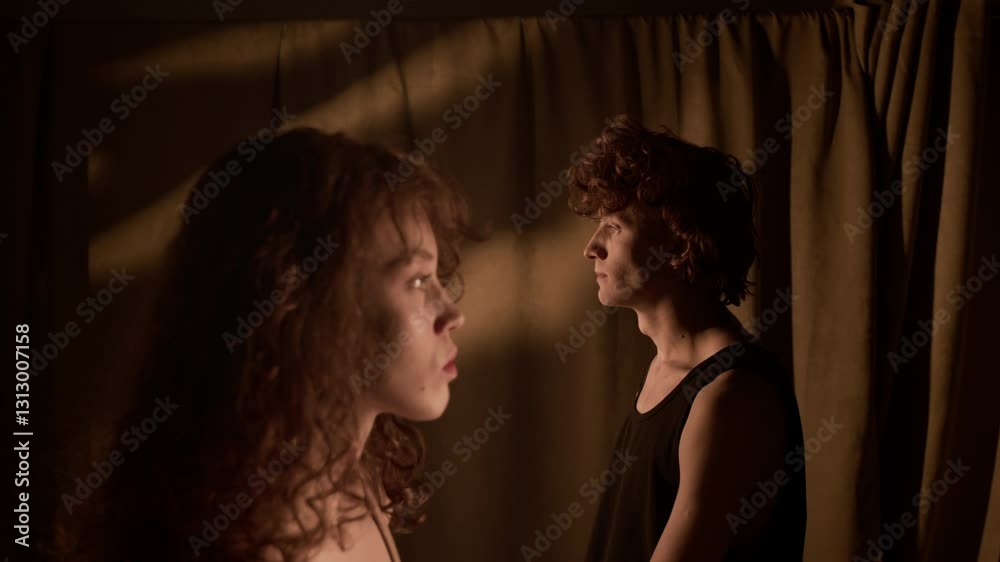 Rack focus portrait of serious curly-haired young woman standing still in foreground, guy dressed in black tank top nodding and looking at camera in background Rack focus portrait of serious curly-haired young woman standing still in foreground, guy dressed in black tank top nodding and looking at camera in background