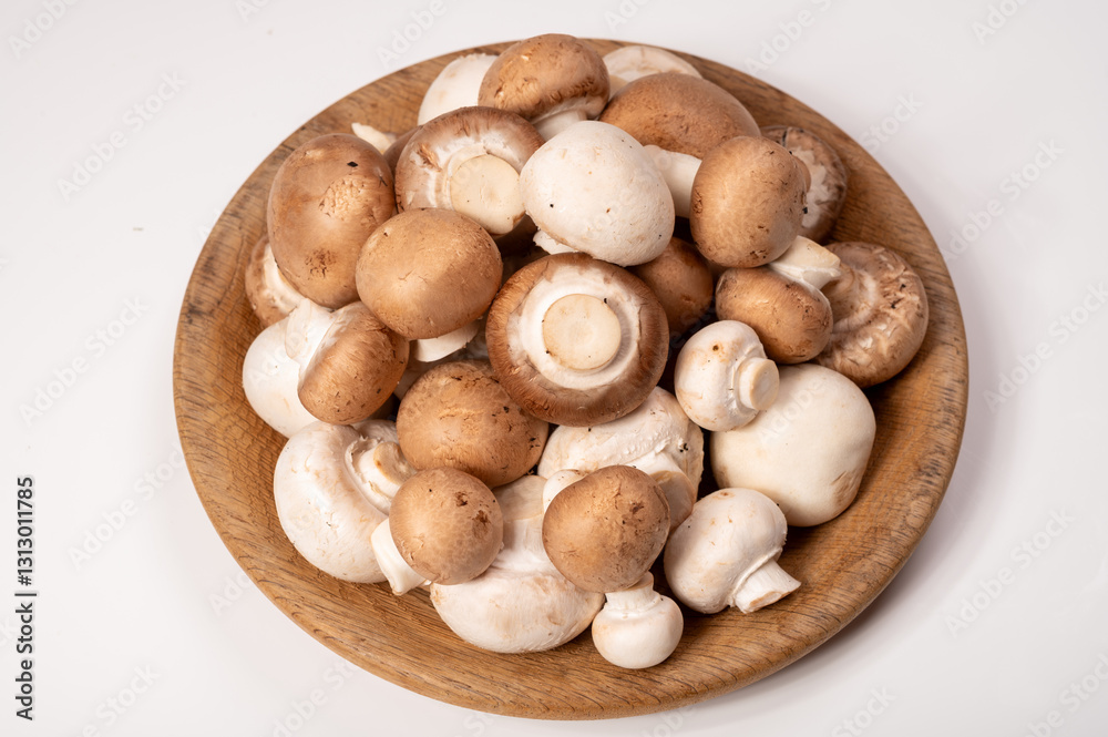 White and brown champignons mushrooms fresh uncooked on wooden plate copy space on white background White and brown champignons mushrooms fresh uncooked on wooden plate copy space on white background