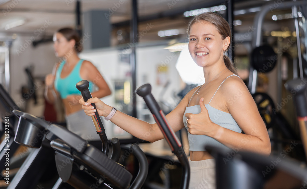 Fototapeta premium Young sporty girl working out on elliptical machine in gym. Healthy active lifestyle concept