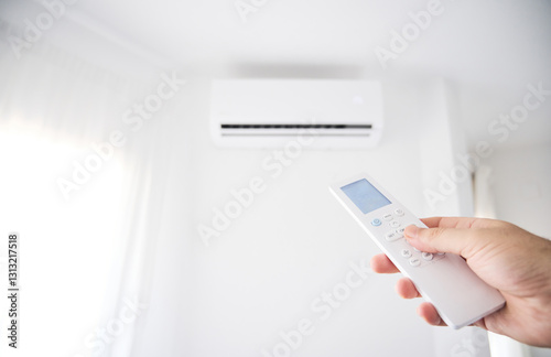 Hand of an unrecognizable person activates an air conditioning unit at home using the remote control