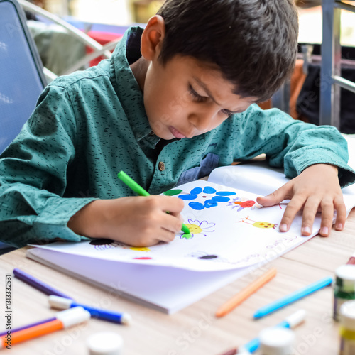 Smart Indian little boy perform thumb painting with different colourful water colour kit during the summer vacations, Cute Indian Kid doing colourful thumb painting drawing on wooden table