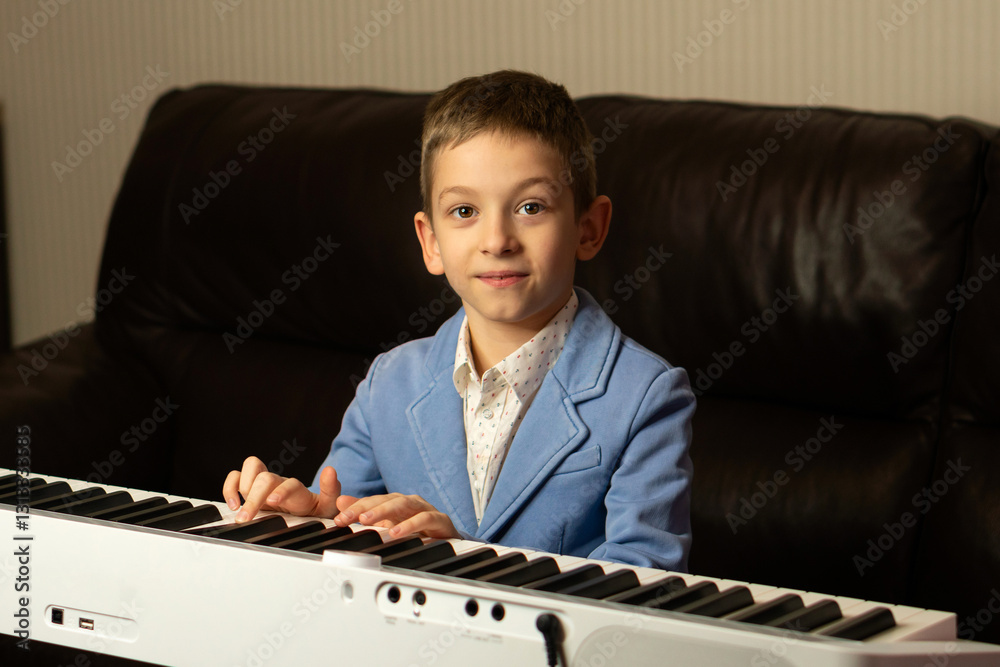 Smiling young boy in a blue blazer playing the piano. Learn piano at home. The concept of education Smiling young boy in a blue blazer playing the piano. Learn piano at home. The concept of education
