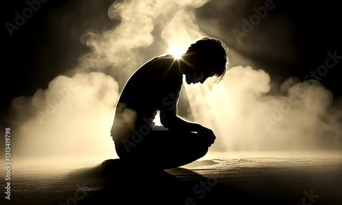 Silhouette of a person kneeling in prayer, bathed in light