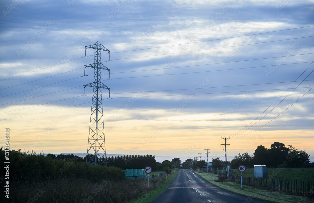 Power pylon and power lines along a country road at sunrise. 80kmh speed sign on the side of road. Taranaki.