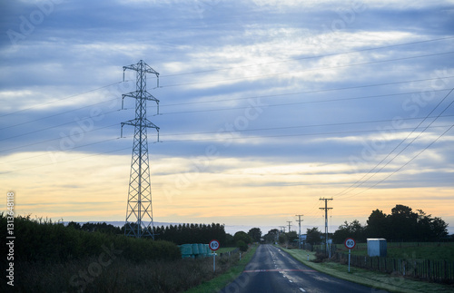 Obraz na płótnie Power pylon and power lines along a country road at sunrise. 80kmh speed sign on the side of road. Taranaki. w salonie
