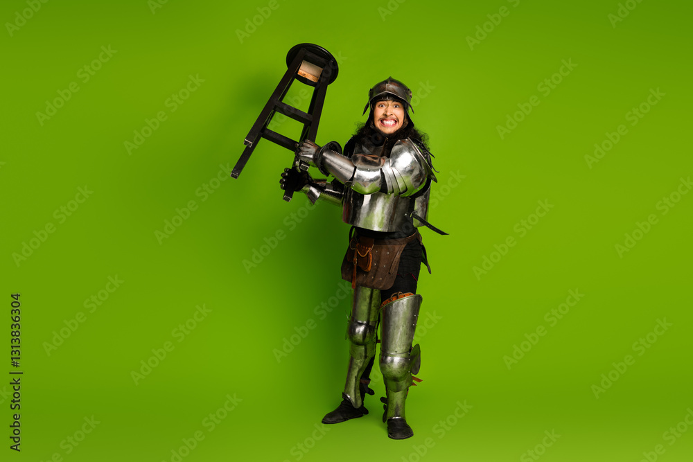 Young man wearing medieval armor posing humorously in front of vibrant green background Young man wearing medieval armor posing humorously in front of vibrant green background