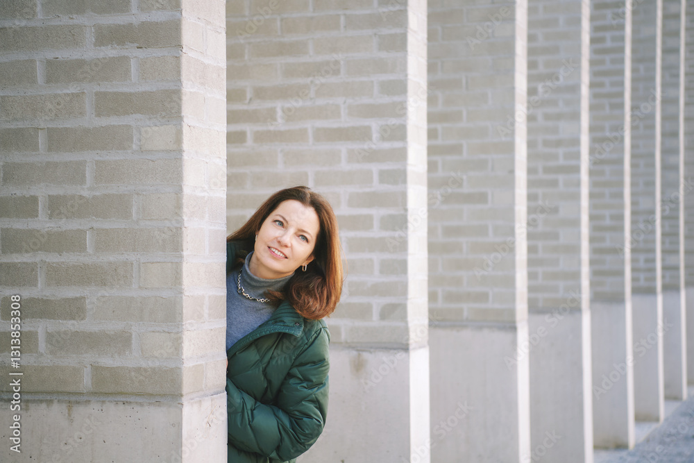 Φωτογραφία Outdoor portrait of middle age woman looking out from behind the wall, wearing w