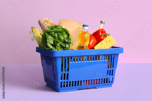 Blue shopping basket full of different fresh products and bottle of oil on lilac background