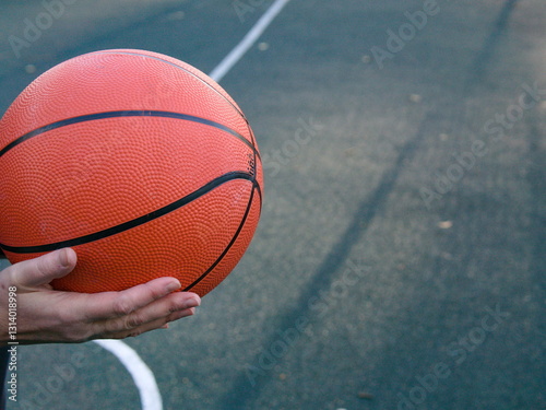 A basketball ball in the hands of an athlete is large on a sports field. Place for the text