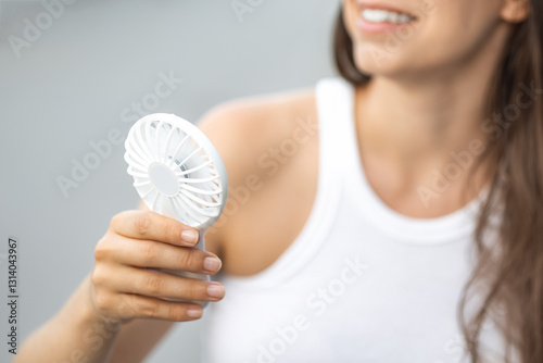woman with white electric hand fan in her hand and air blowing over her smiles with white teeth. Concept: Escape from the heat electric mini hand fan. no face. Strong hot summer days. close-up