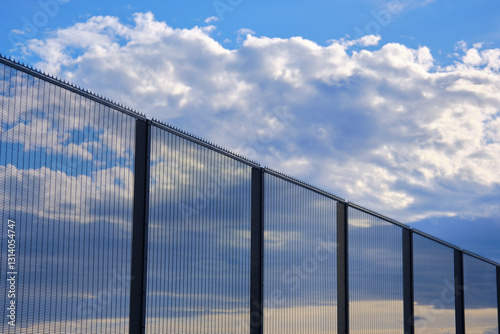 High security fence reflecting clouds and blue sky
