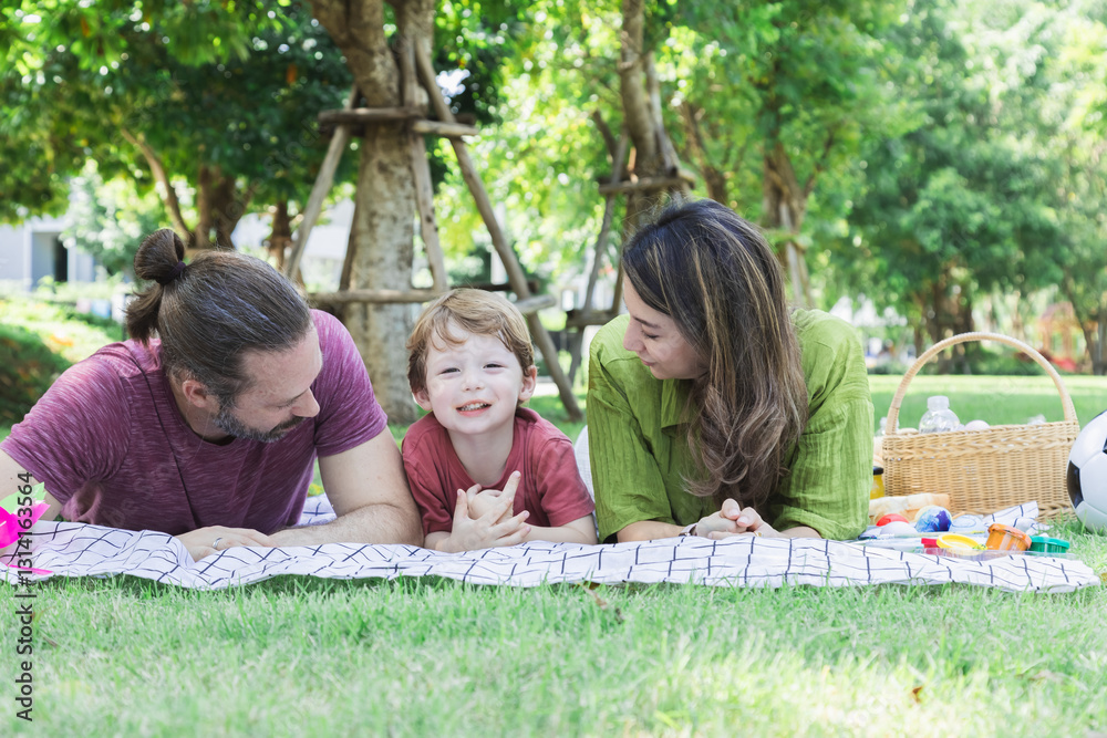 Fototapeta premium Hispanic or Caucasian family outdoor activities lifestyle, Mother, father and little boy lying down on grass happy kissing and embracing with love and tender, toddler playing with mom and dad in park