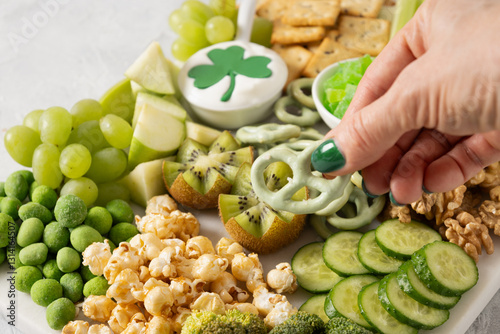 Obraz na płótnie St Patricks day charcuterie board decorated shamrock and clover leaf. Festive holiday appetizer for celebration. Female hands dip cracker to sauce. Close up w salonie