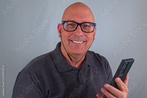 A smiling man against a white backdrop is smiling while listening to an audiobook on his cell phone. photo