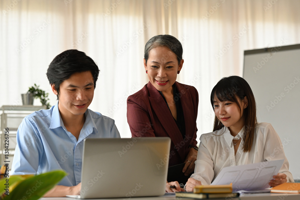A senior professional provides insights to two young business people as they review project drafts A senior professional provides insights to two young business people as they review project drafts
