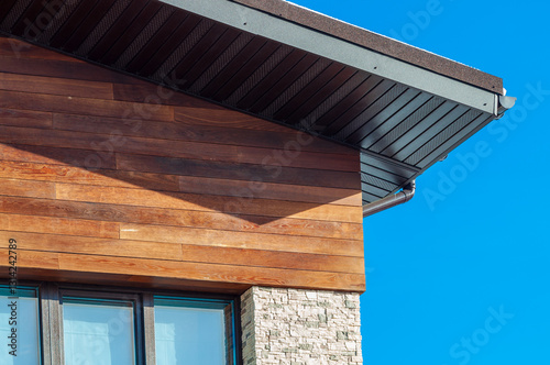 Close-up of a modern building's wood siding and stone foundation against a vibrant blue sky.