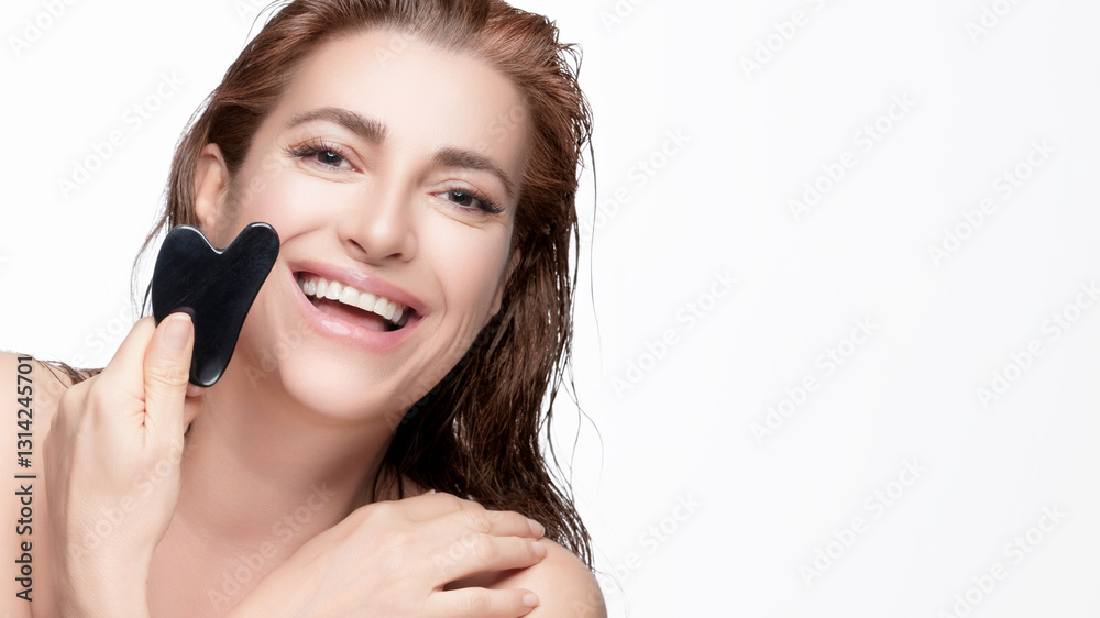 Smiling woman using a gua sha tool for skincare on white background