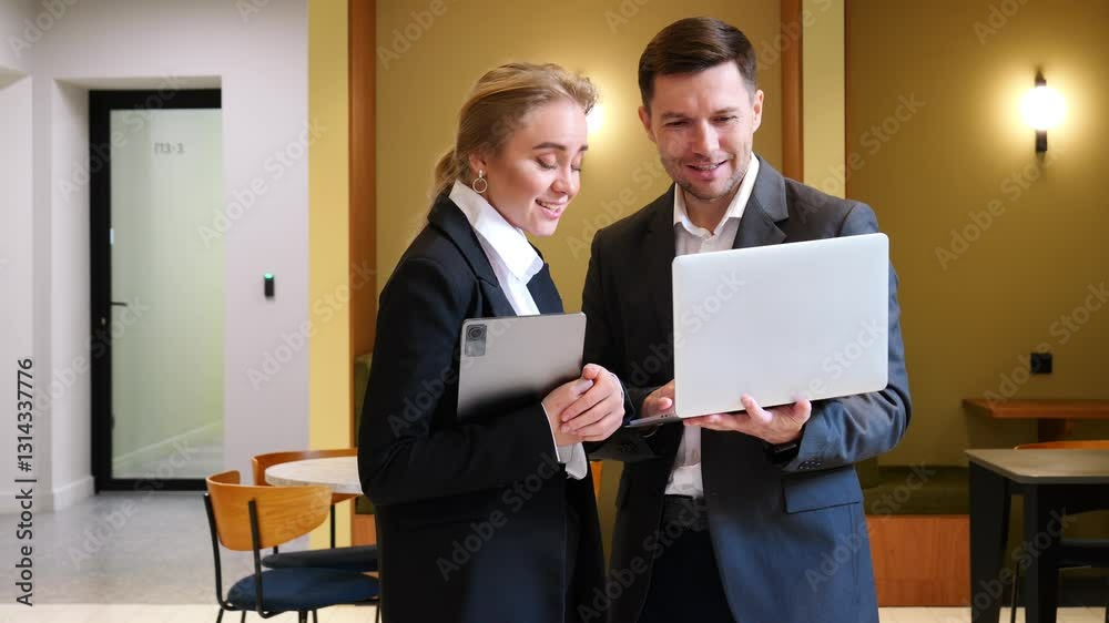 The two professionals exchange smiles as they discuss information on the laptop in their stylish workspace. The two professionals exchange smiles as they discuss information on the laptop in their stylish workspace.