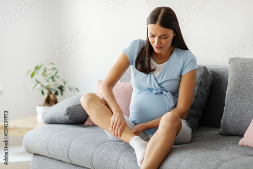Problems with health during pregnancy. Young expecting lady massaging her swollen foot, sitting on sofa at home