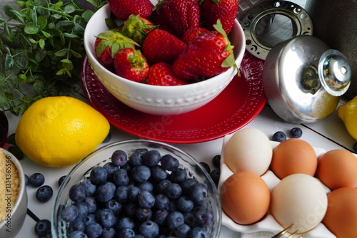Baking a fresh classic cheesecake with a hint of lemon and topped with fresh strawberries and blueberries for a birthday party.  New York style cheesecake topped with berries on a white background.