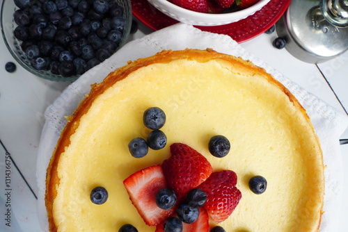 Baking a fresh classic cheesecake with a hint of lemon and topped with fresh strawberries and blueberries for a birthday party.  New York style cheesecake topped with berries on a white background.
