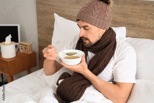 Ill young man eating soup i...