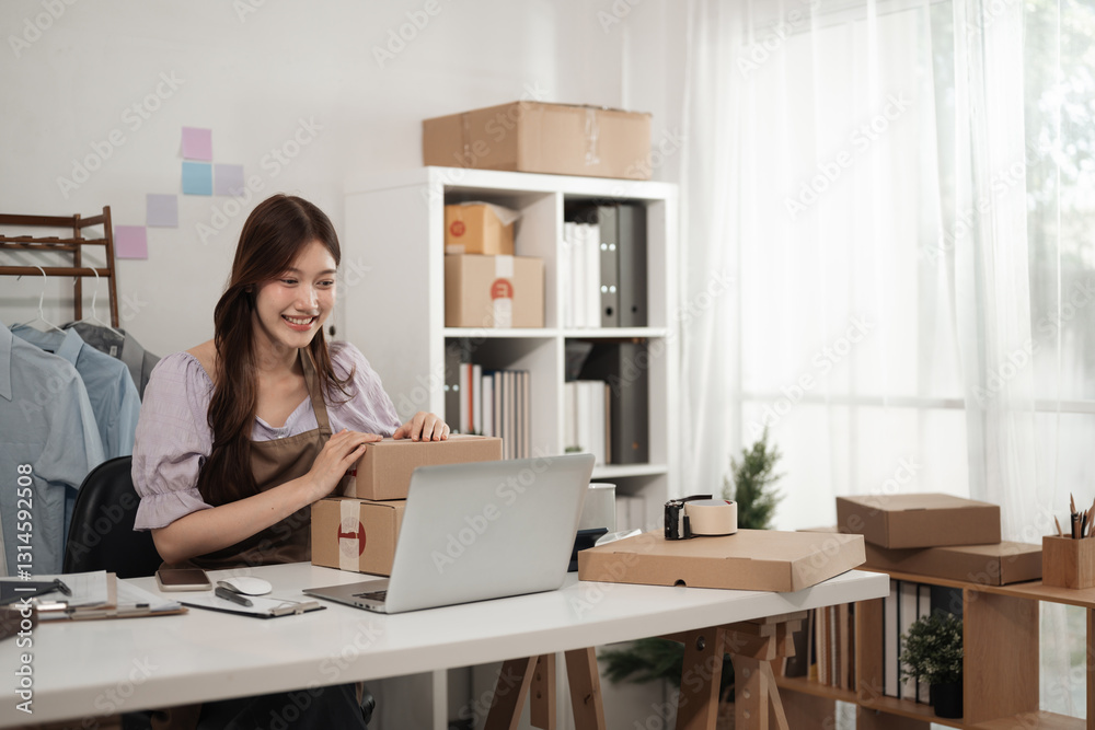 A cheerful small business owner in an apron interacts with her laptop while handling packed boxes, A Happy Seller at Work, Online Business Success A cheerful small business owner in an apron interacts with her laptop while handling packed boxes, A Happy Seller at Work, Online Business Success