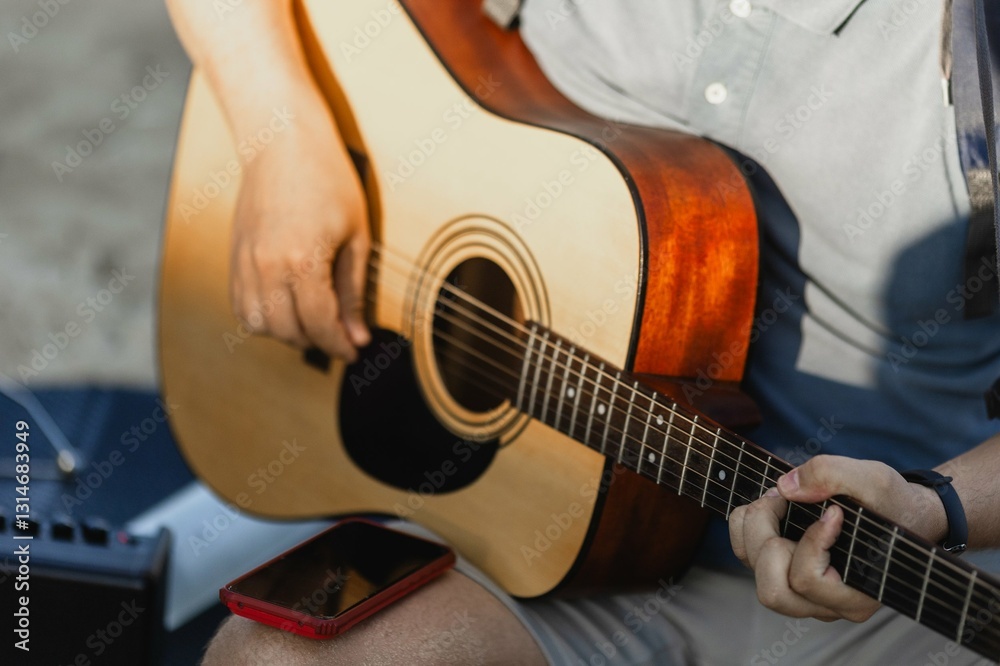 Fototapeta premium Young caucasian male playing acoustic guitar outdoors